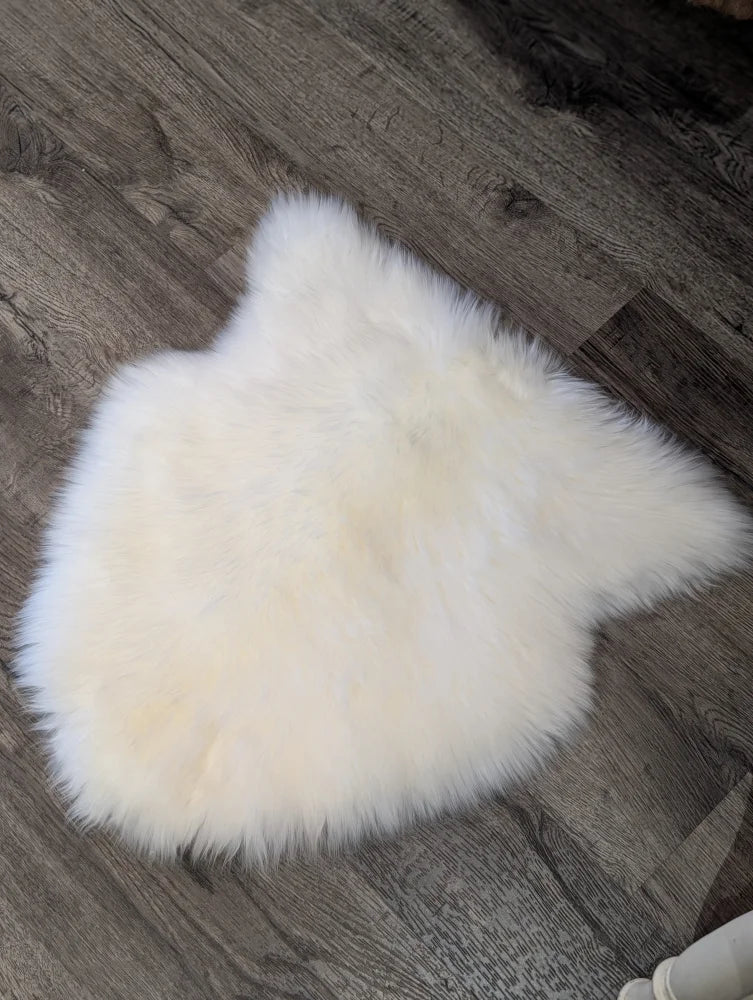 A large off-white merino sheepskin chair pad with a soft fluffy texture on a dark wood floor perfect as chair pads