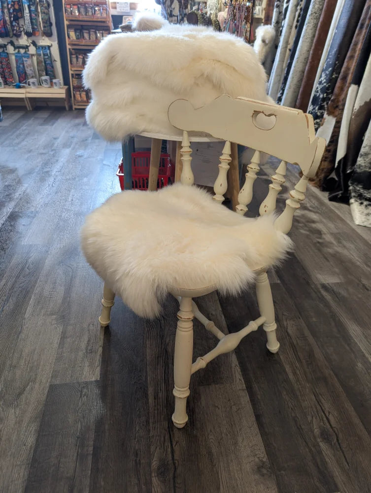 Cream-colored wooden chair with fluffy white merino sheepskin chair pads on seat and backrest for extra comfort