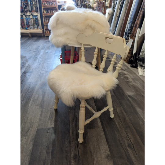 Cream-colored wooden chair with fluffy white merino sheepskin chair pads on seat and backrest for extra comfort