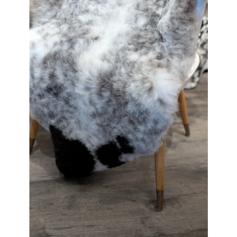 A plush gray and white large dalmatian icelandic sheepskin rug draped over a chair with wooden legs short wool icelandic
