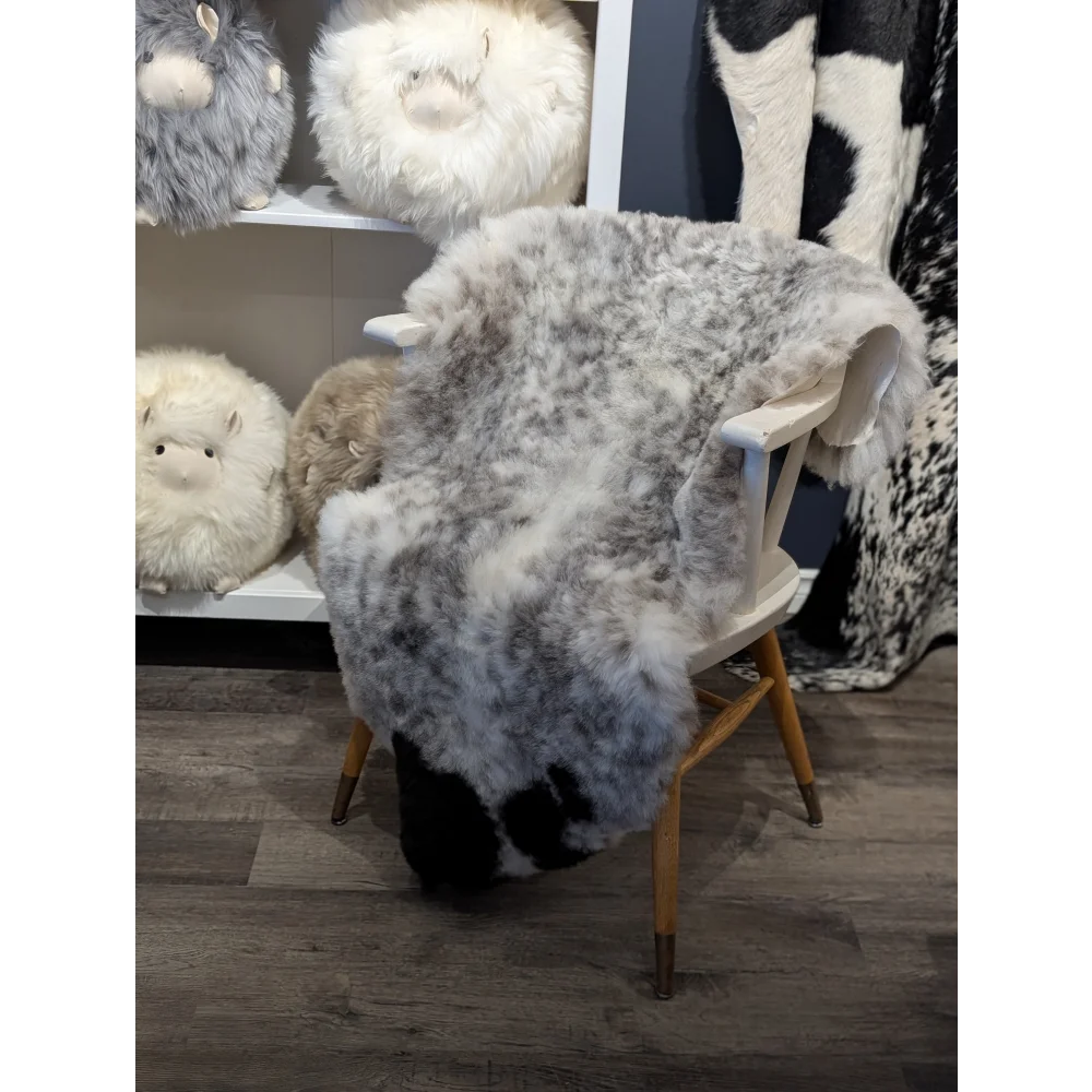 A soft gray and white speckled large icelandic sheepskin rug made of short wool draped over a wooden chair