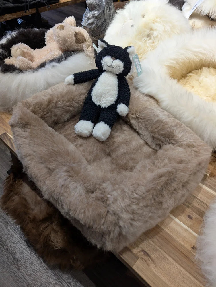 Cute black and white plush monkey toy with pom-pom tail on sheepskin pet bed