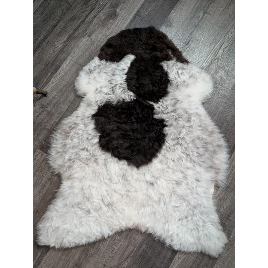 A plush spotted icelandic sheepskin rug with soft white wool and black patches in a natural abstract pattern