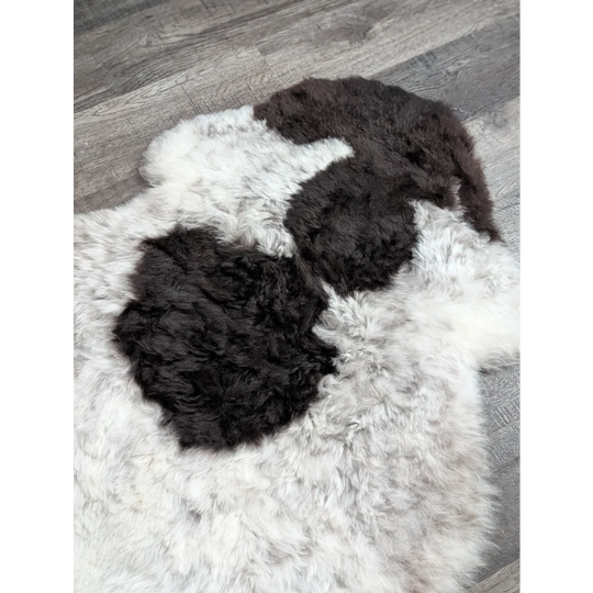 A large soft spotted icelandic sheepskin rug with natural white wool and two dark black patches of fur