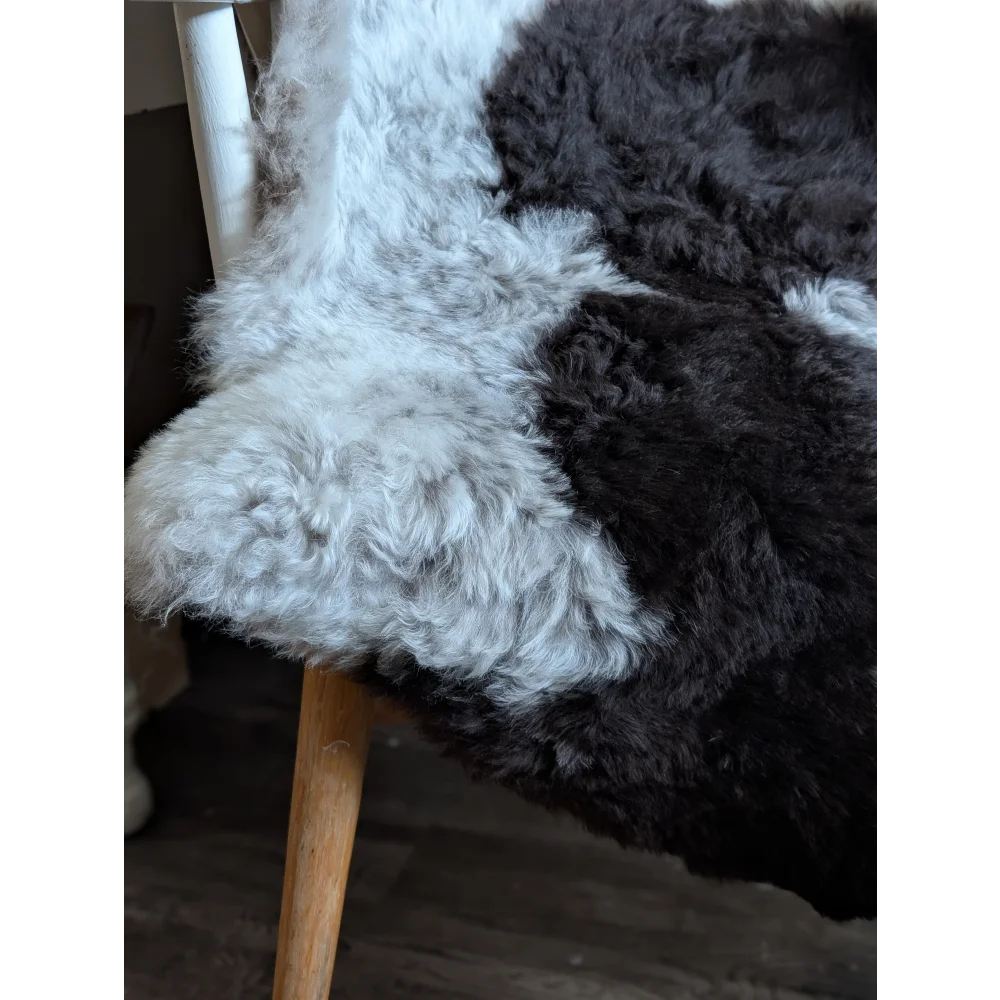 A plush two-toned soft spotted icelandic sheepskin rug in white and dark gray draped over a wooden chair leg