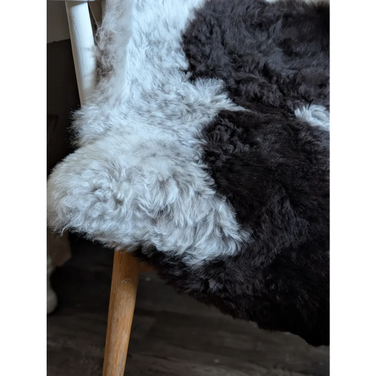 A plush two-toned soft spotted icelandic sheepskin rug in white and dark gray draped over a wooden chair leg