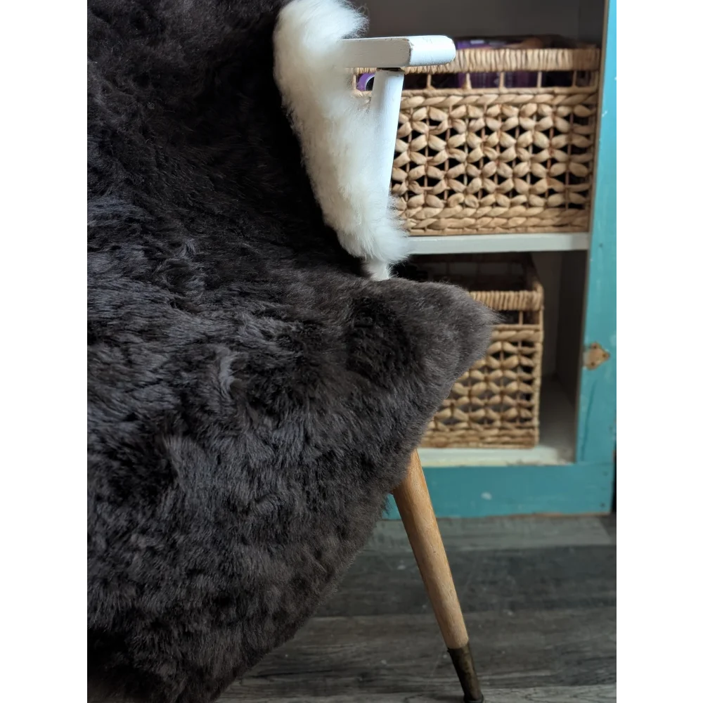 Dark gray plush icelandic sheepskin rug with short wool draped over a white wooden chair with tapered legs
