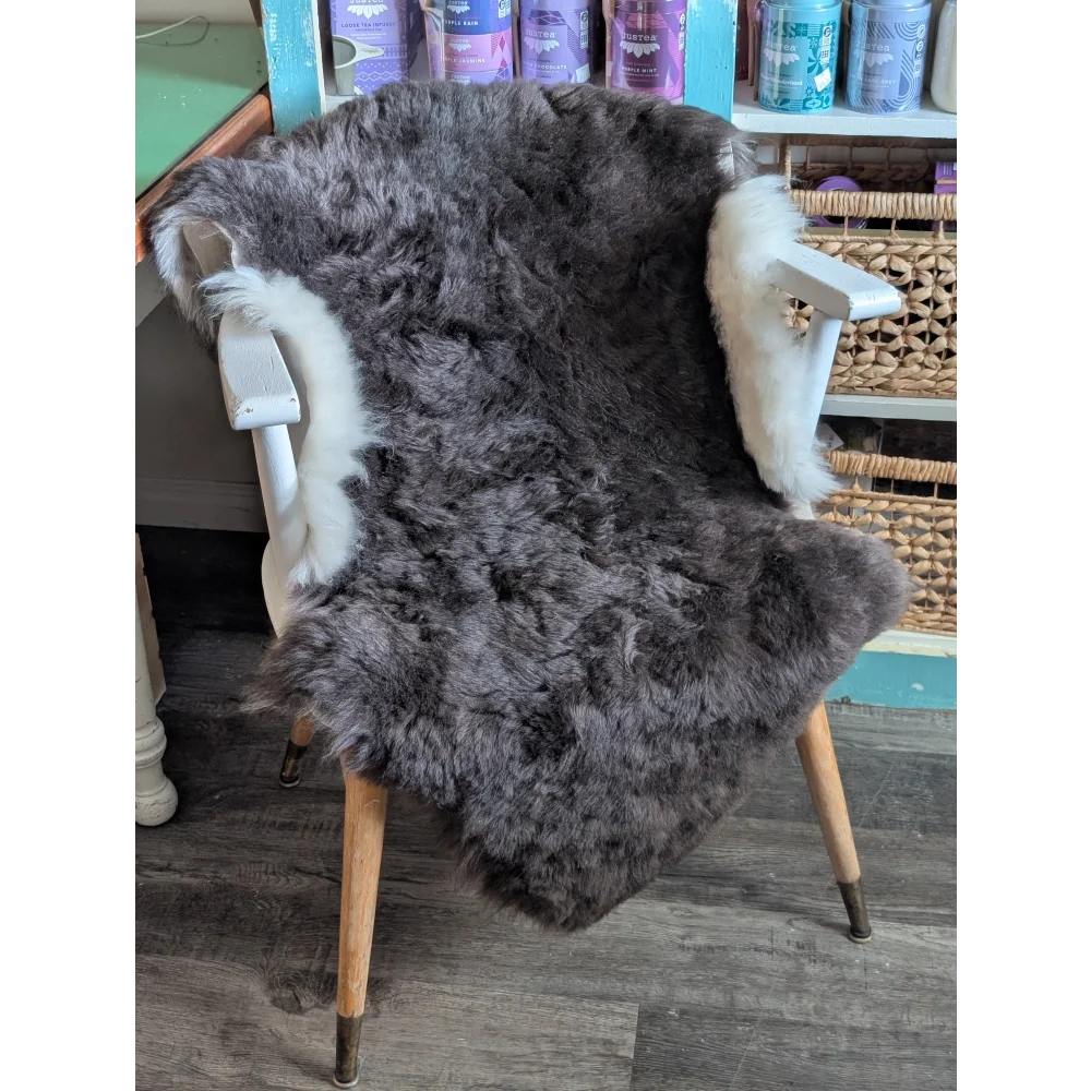 A plush dark gray icelandic sheepskin rug with soft short wool and white fur trim draped over a wooden chair back