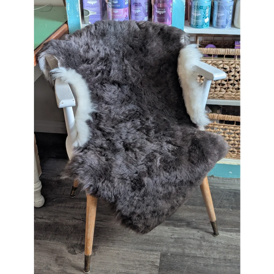 A plush dark gray icelandic sheepskin rug with soft short wool and white fur trim draped over a wooden chair back