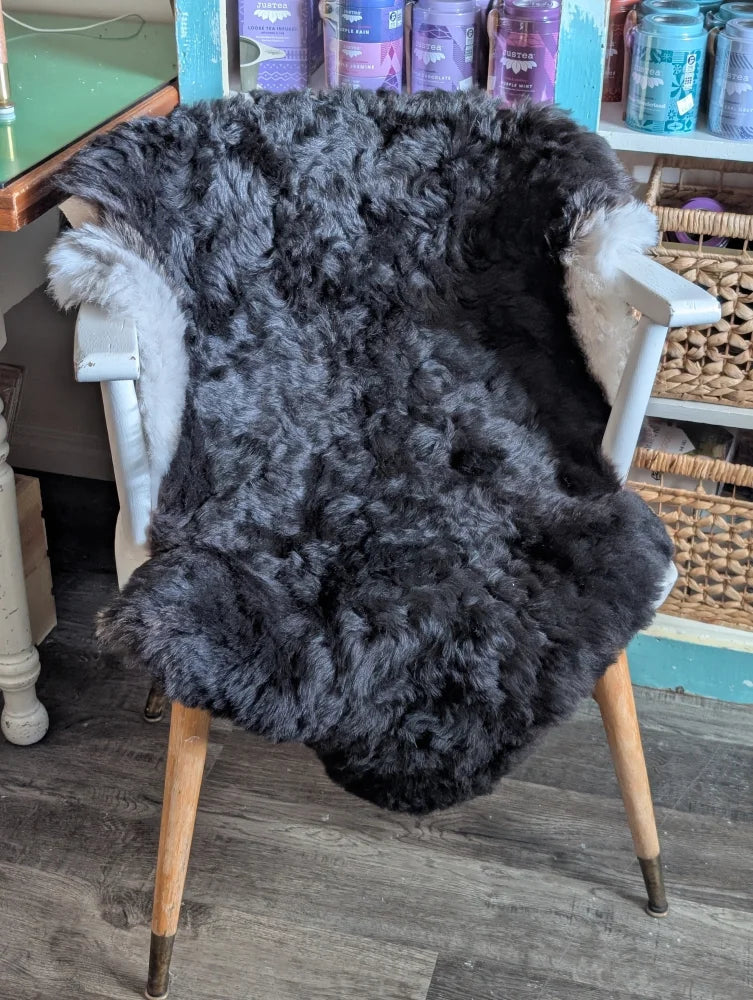 A large soft blacky icelandic sheepskin rug with short wool draped over a white wooden chair
