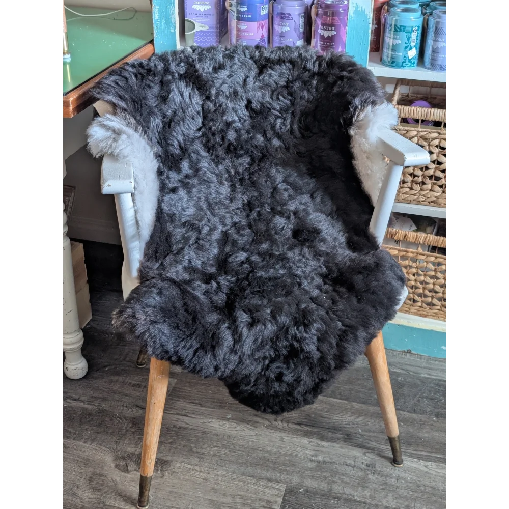 A large soft blacky icelandic sheepskin rug with short wool draped over a white wooden chair