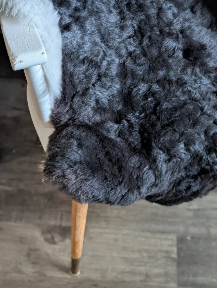 A plush dark gray icelandic sheepskin throw with short wool draped over a white chair with wooden legs
