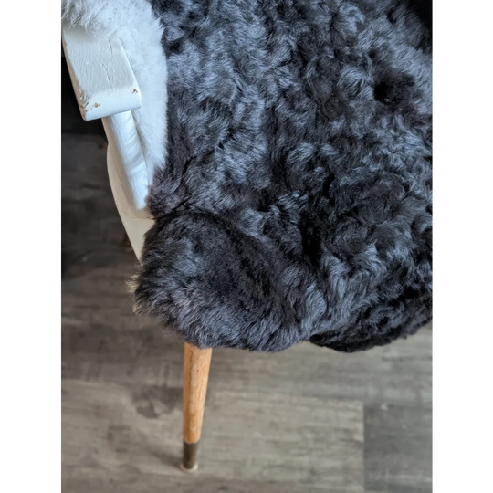 A plush dark gray icelandic sheepskin throw with short wool draped over a white chair with wooden legs
