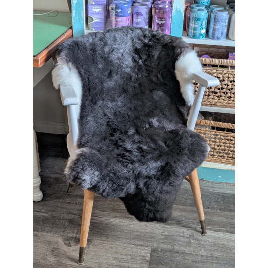 A plush dark gray and white icelandic sheepskin rug with short wool draped over a wooden chair backrest