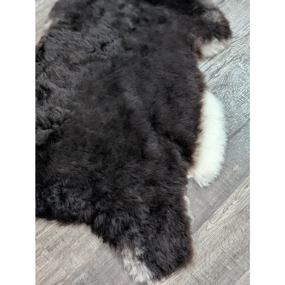 A large soft black and white icelandic sheepskin rug with curly short wool texture sized 43 by 30 inches