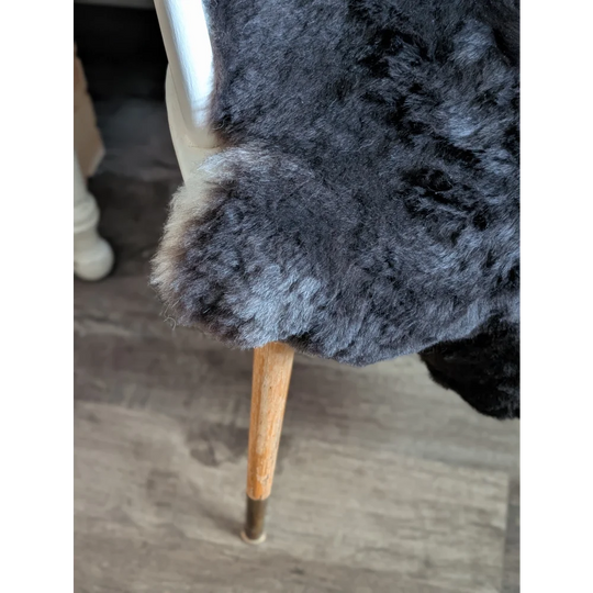 A plush dark gray icelandic sheepskin throw with short wool draped over the back of a chair for cozy use