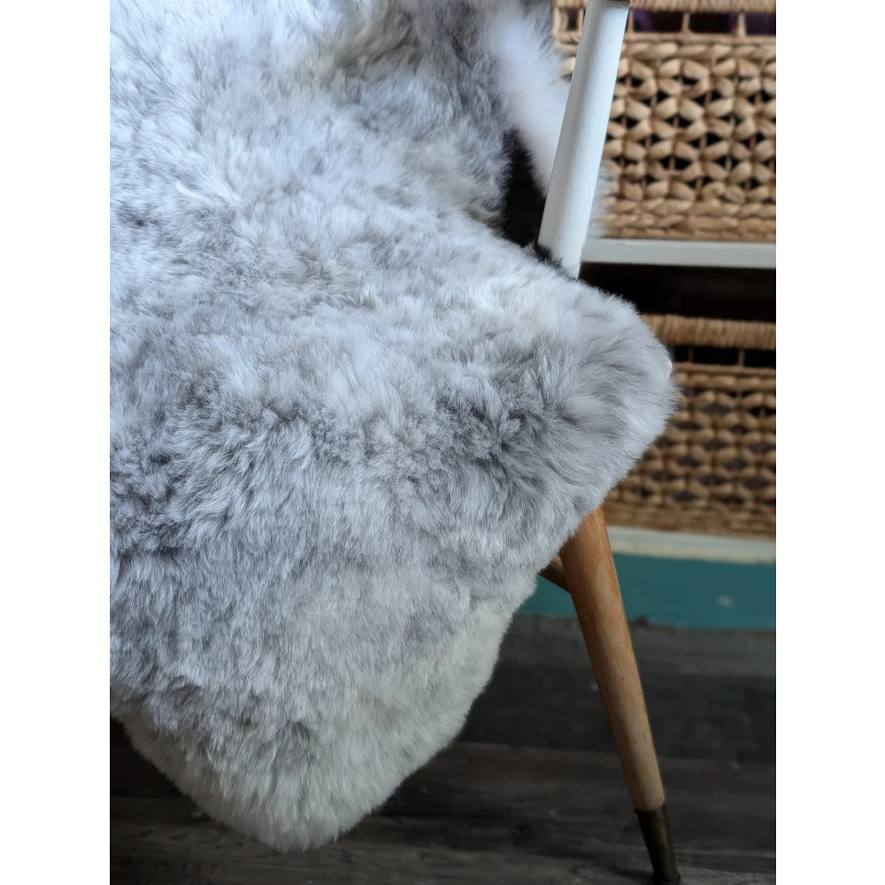 A large soft medium spotted icelandic sheepskin rug in gray draped over a chair leg showing fluffy short wool texture