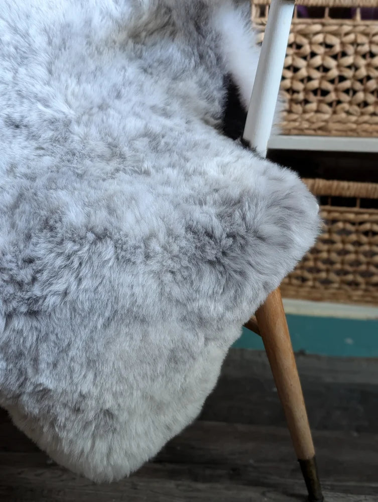 A large soft medium spotted icelandic sheepskin rug in gray draped over a chair leg showing fluffy short wool texture