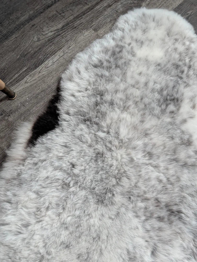 A plush irregular gray spotted icelandic sheepskin rug with soft fluffy texture and natural shade variations
