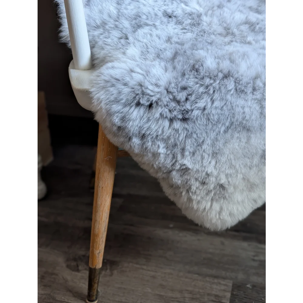 A plush light gray spotted icelandic sheepskin throw draped over a chair back with short soft wool texture