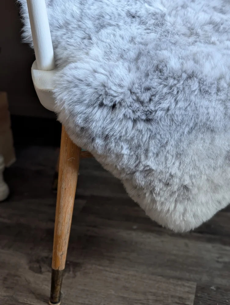 A plush light gray spotted icelandic sheepskin throw draped over a chair back with short soft wool texture