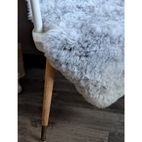 A plush light gray spotted icelandic sheepskin throw draped over a chair back with short soft wool texture