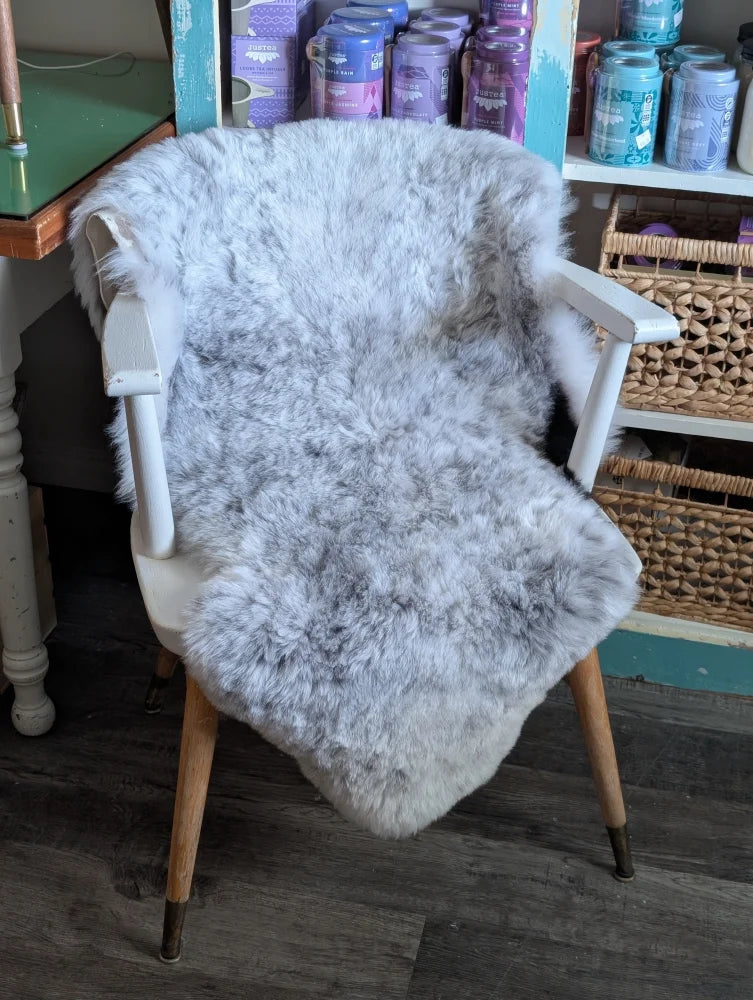 A soft light gray spotted icelandic sheepskin rug draped over a white wooden chair with tapered legs