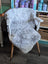 A soft light gray spotted icelandic sheepskin rug draped over a white wooden chair with tapered legs