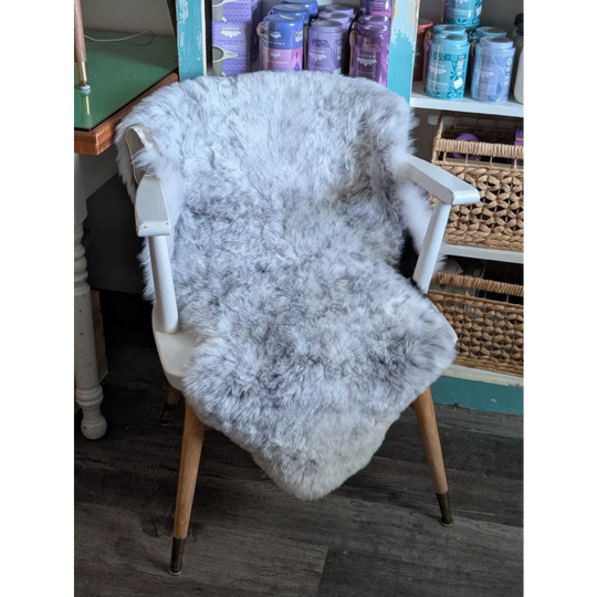 A soft light gray spotted icelandic sheepskin rug draped over a white wooden chair with tapered legs