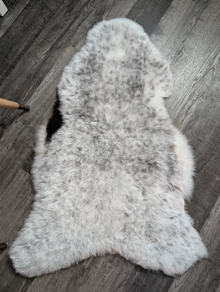 A plush spotted icelandic sheepskin rug with soft gray and white fur in a natural shape measuring 43 by 26 inches