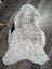 A plush spotted icelandic sheepskin rug with soft gray and white fur in a natural shape measuring 43 by 26 inches