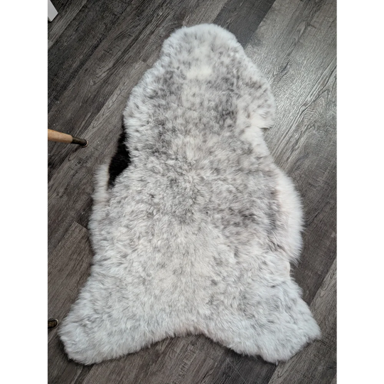 A plush spotted icelandic sheepskin rug with soft gray and white fur in a natural shape measuring 43 by 26 inches