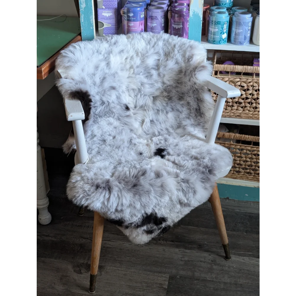 A plush gray and black speckled spotted icelandic sheepskin rug draped over a white wooden armchair with light wood legs