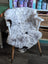 A plush gray and black speckled spotted icelandic sheepskin rug draped over a white wooden armchair with light wood legs