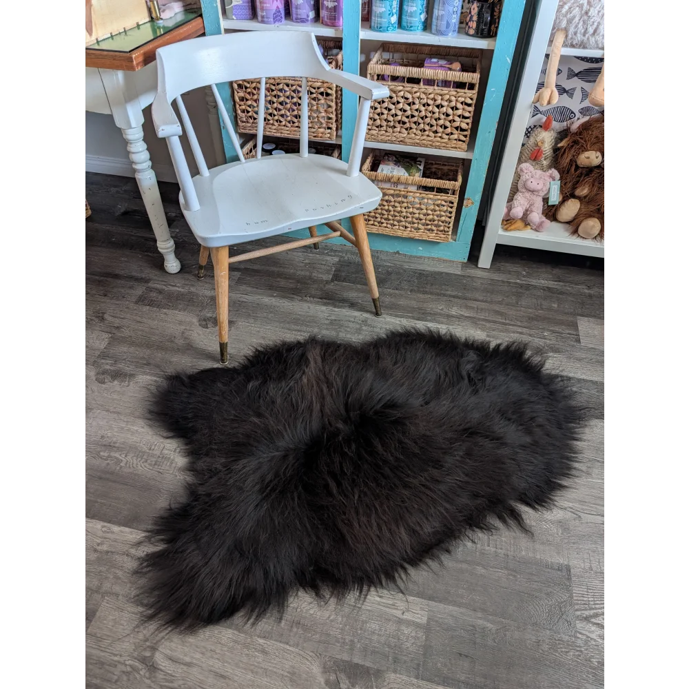 A plush black icelandic sheepskin rug with long wool lies on the floor perfect for cozy decor