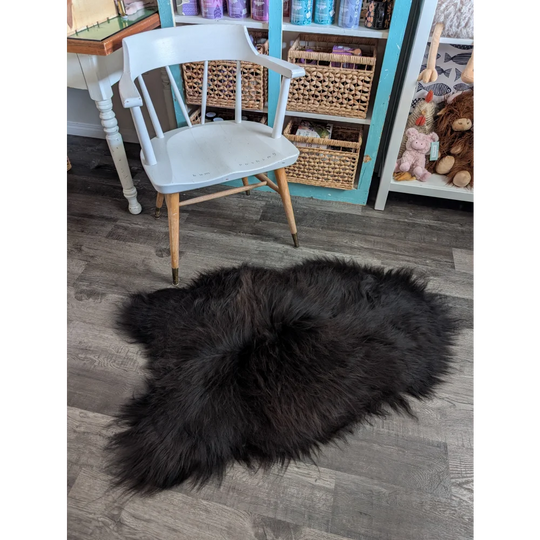 A plush black icelandic sheepskin rug with long wool lies on the floor perfect for cozy decor