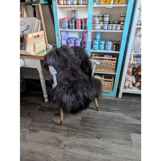 Black fluffy large chair with light wooden legs and white armrests made from long wool icelandic sheepskin