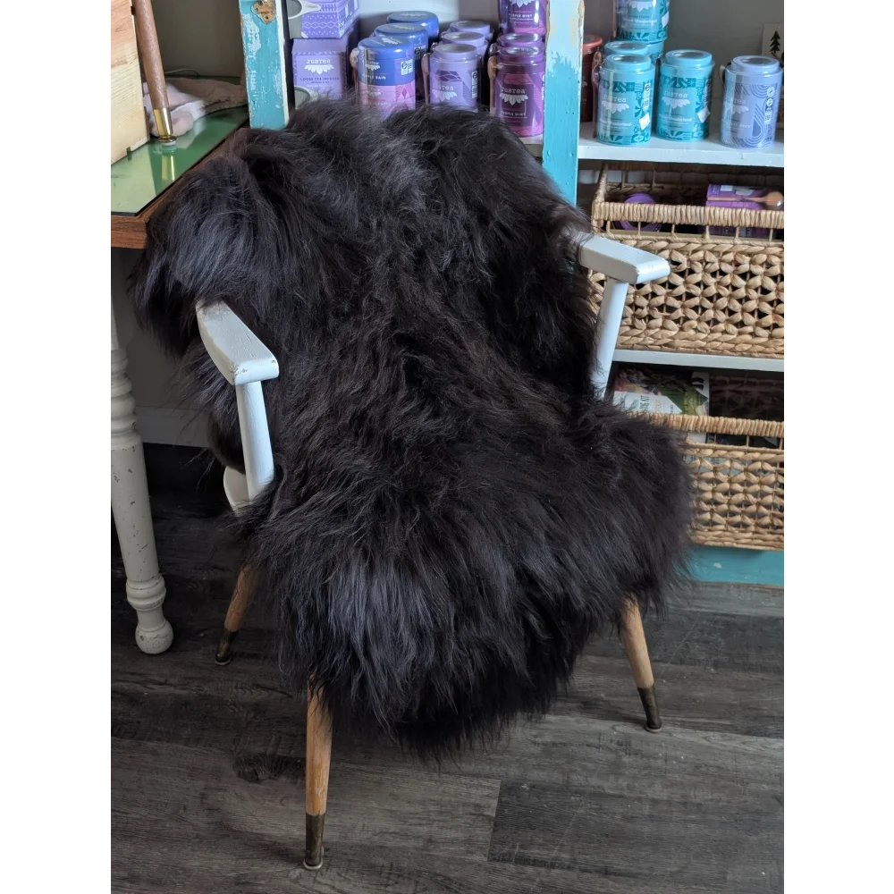 A plush black icelandic sheepskin with long wool draped over a white wooden chair with light wood legs