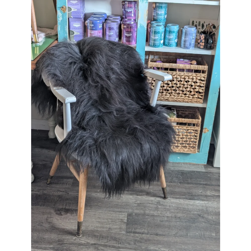 A plush dark gray icelandic sheepskin rug with long wool draped over a white wooden chair with light wood legs