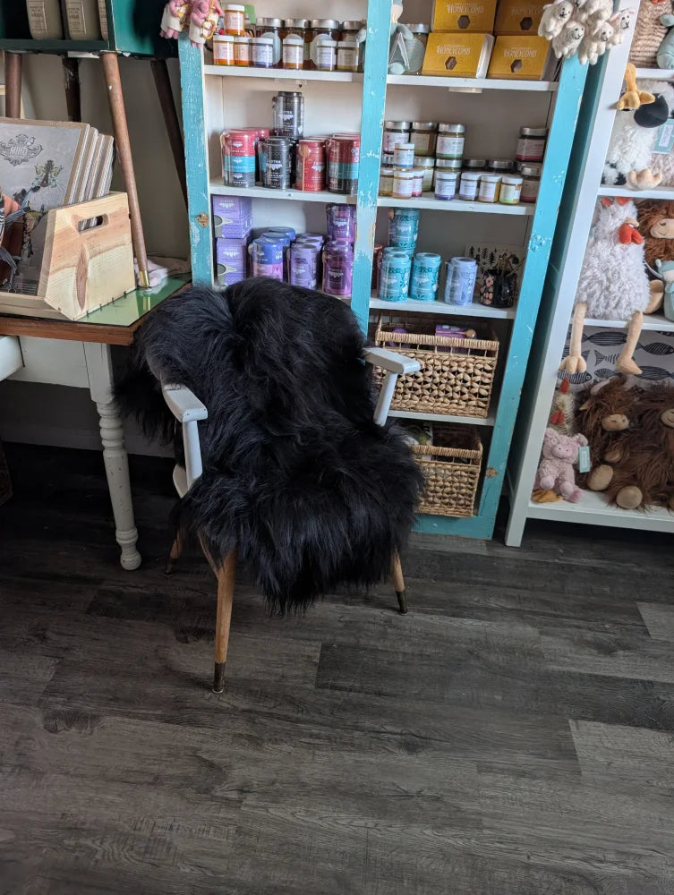 A large soft black icelandic sheepskin throw with long wool draped over a white wooden chair with light brown legs