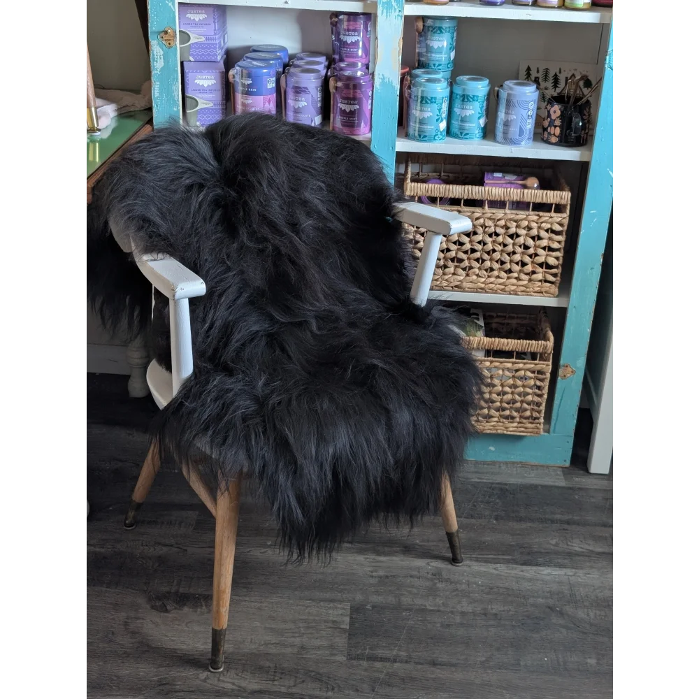 Black thick-furred icelandic sheepskin throw draped over white wooden chair with light wood legs, long wool icelandic style