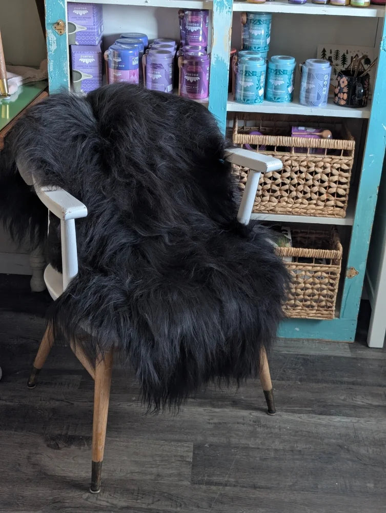 Black thick-furred icelandic sheepskin throw draped over white wooden chair with light wood legs, long wool icelandic style