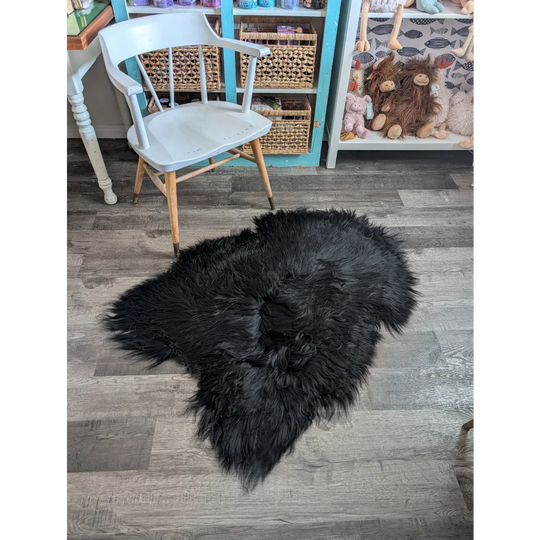 Black fluffy icelandic sheepskin rug with long wool in natural irregular shape soft dense fur for cozy decor