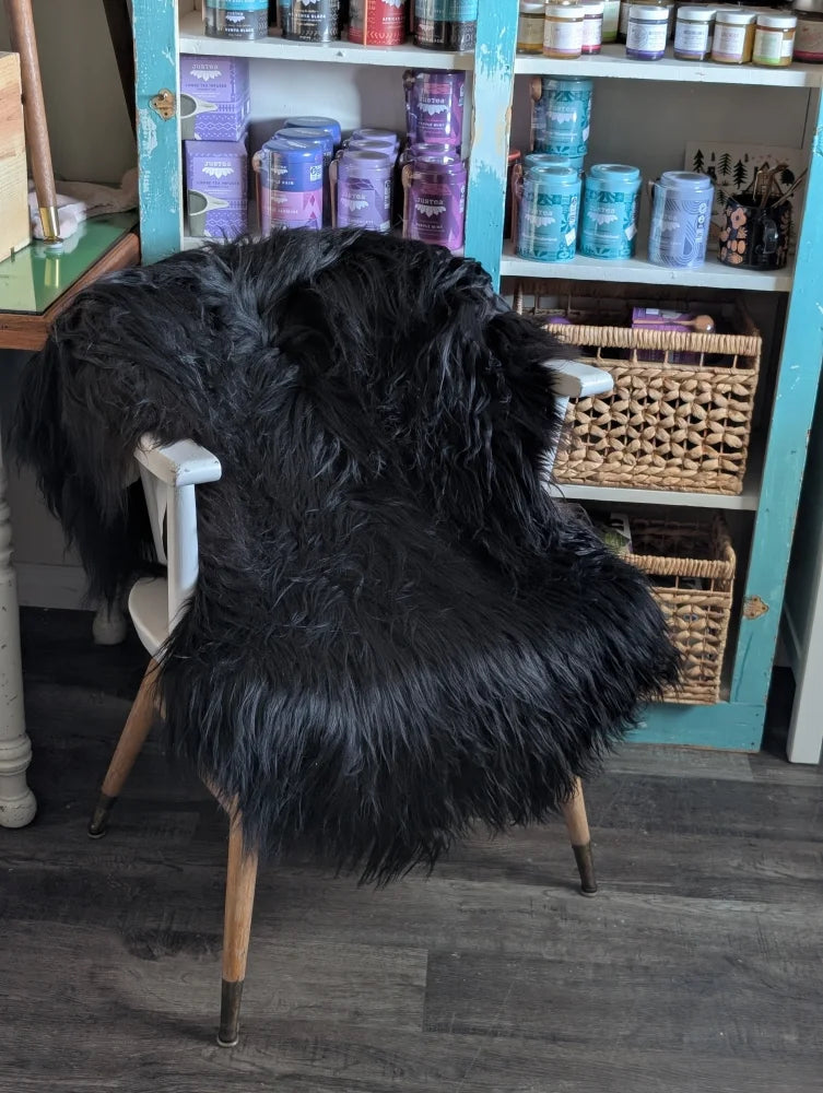 Black thick-furred long wool icelandic sheepskin chair cover draped over white wooden chair with metal legs