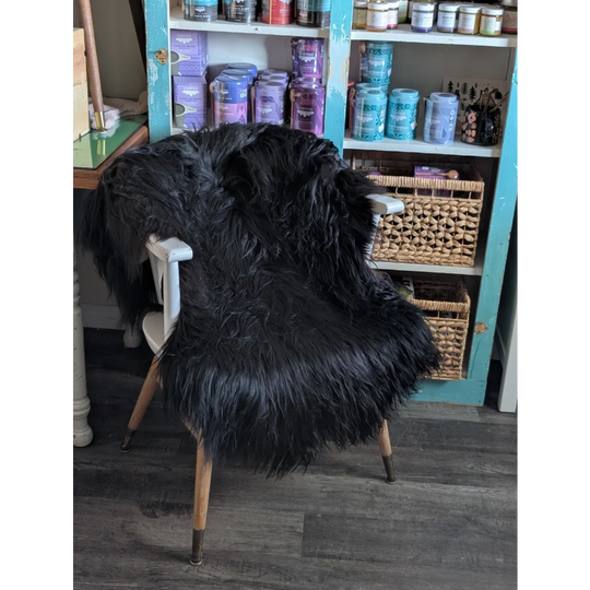 Black thick-furred long wool icelandic sheepskin chair cover draped over white wooden chair with metal legs