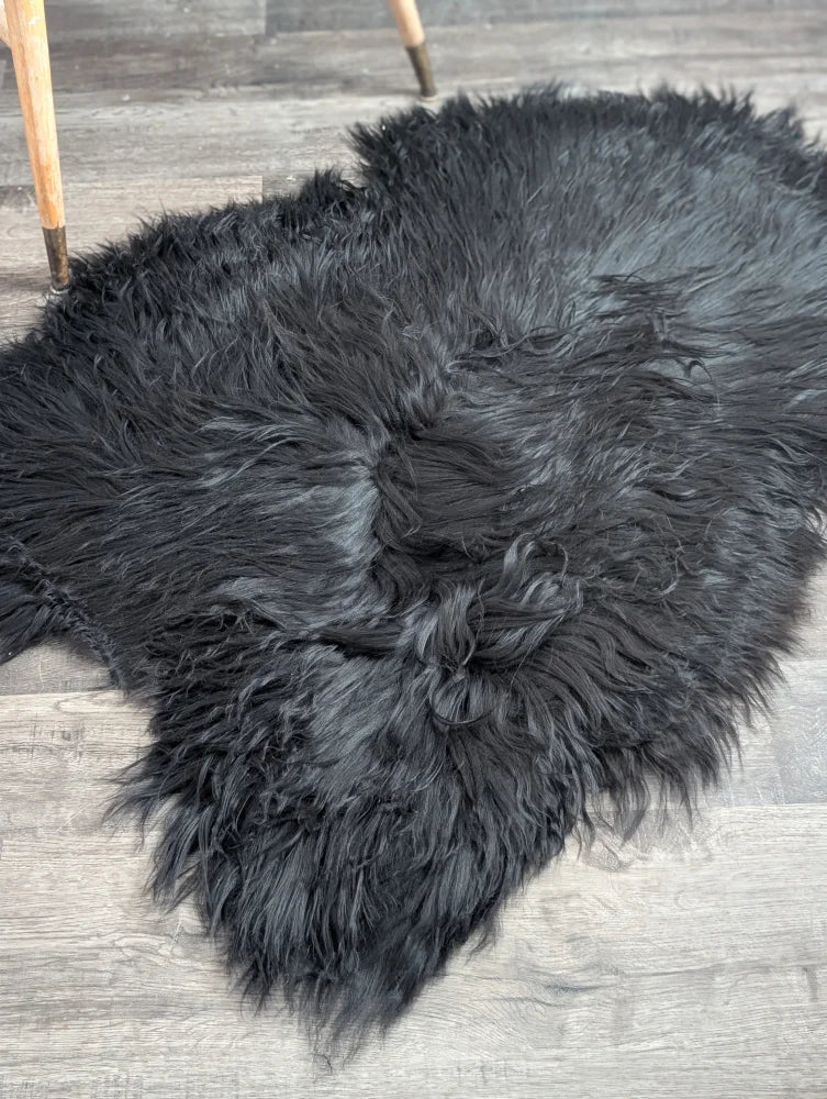 Black fluffy large soft icelandic sheepskin rug with long wool and natural irregular shape in black color