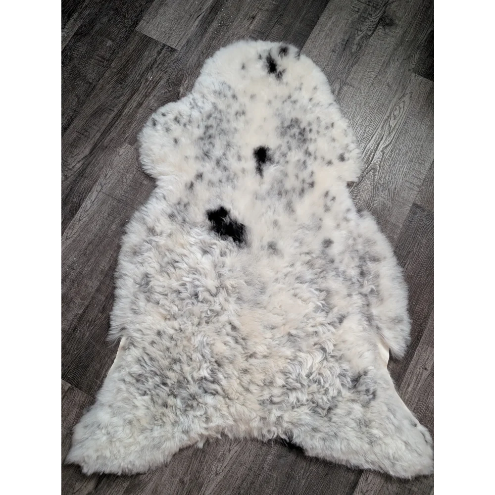 A plush spotted icelandic sheepskin rug with soft white wool and medium black patches perfect for cozy decor