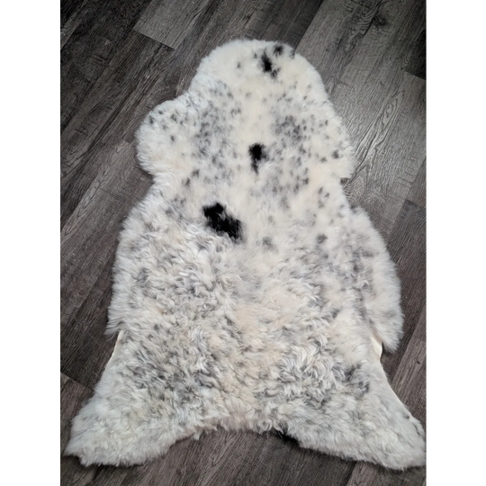 A plush spotted icelandic sheepskin rug with soft white wool and medium black patches perfect for cozy decor