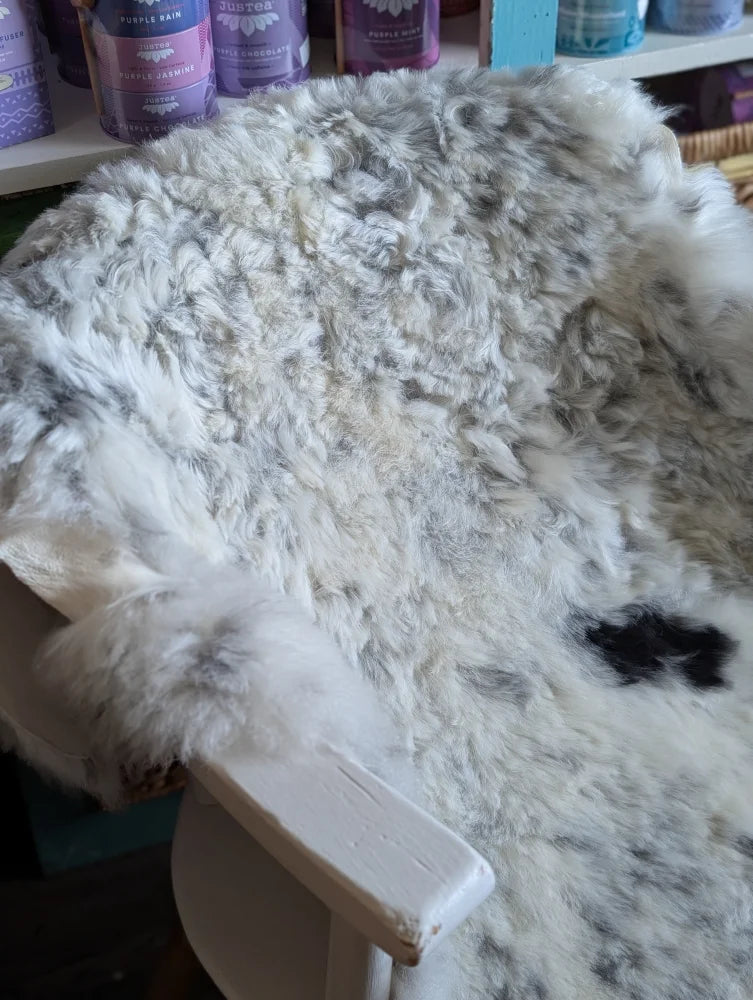 A large spotted icelandic sheepskin rug with white and gray speckles draped over a rustic wooden chair arm