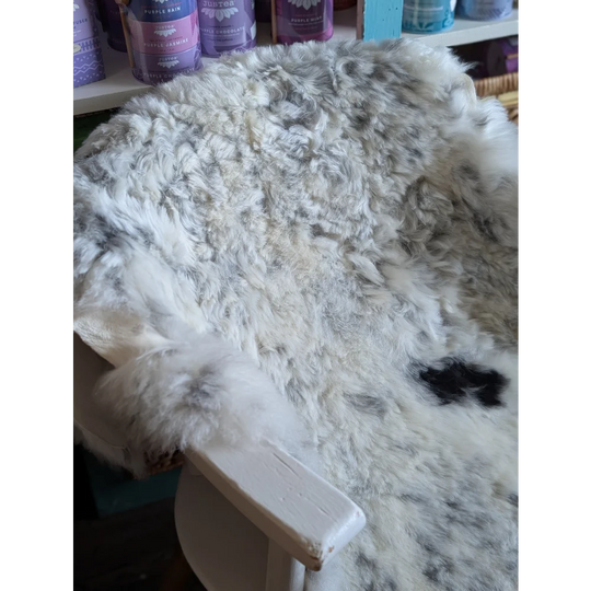 A large spotted icelandic sheepskin rug with white and gray speckles draped over a rustic wooden chair arm